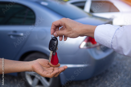 The male sales man is sending the keys and the car to the customer after agreeing to buy and sell the car.  Concept for car rental