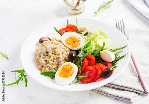 Breakfast oatmeal porridge with greek salad of tomatoes, cucumbers, olives and eggs. Healthy balanced food.