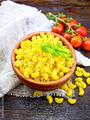 Elbow macaroni in bowl with tomatoes on board