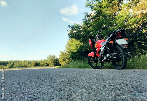 red motorcycle stands on the road alone near the forest
