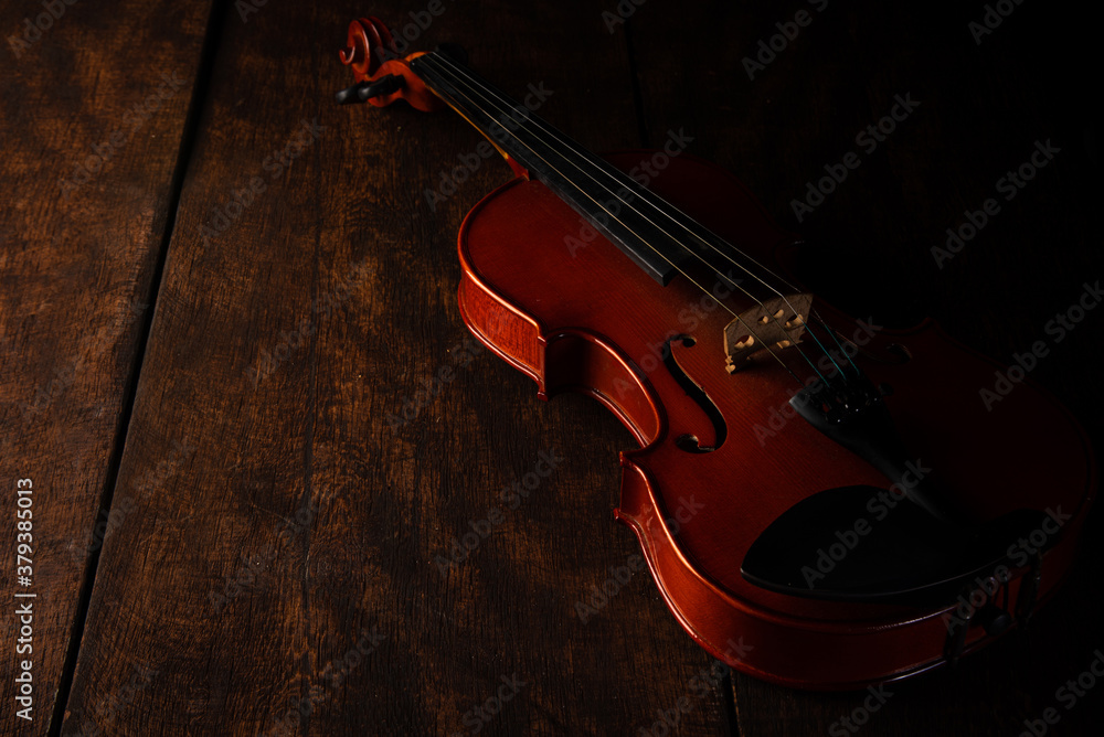 Old and beautiful violin on a rustic wooden surface and black background low key portrait, selective focus. Old and beautiful violin on a rustic wooden surface and black background low key portrait, selective focus.