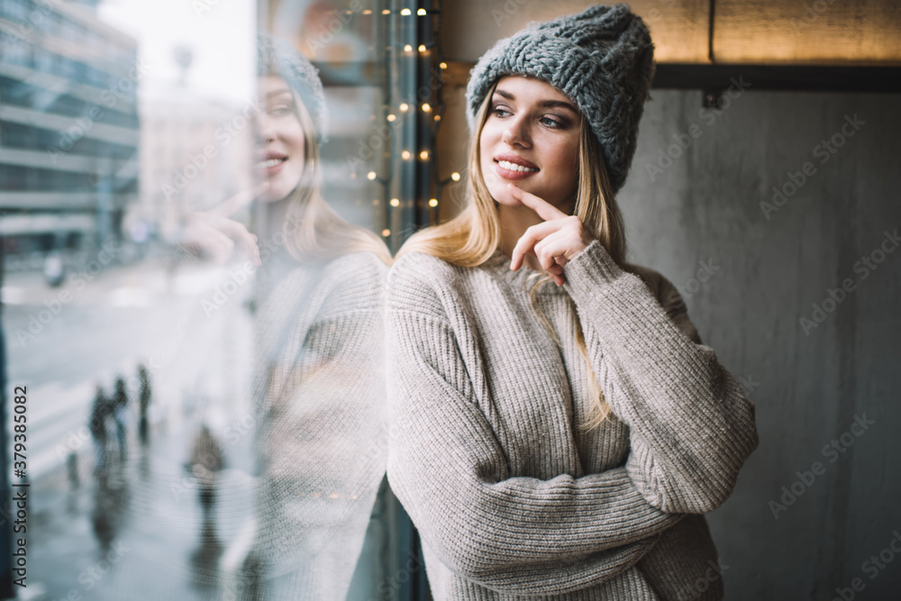 Contemplative female teenager dressed in stylish winter hat and knitted sweater looking at window and dreaming, happy Caucasian hipster girl 20 years old enjoying recreation and youth lifestyle - obrazy, fototapety, plakaty 