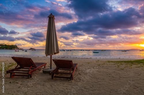 Colorful sunrise at lonely beach of Praslin island with two wooden resting chairs and umbrella, Seychelles photo