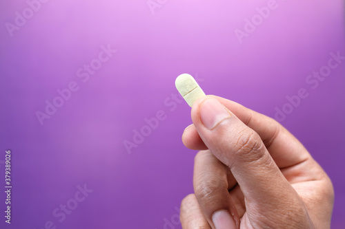 hand holding pills on purple background with copy space 