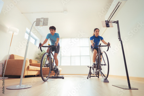 Asian couple. They are exercising in the home.By cycling on the trainer and play online bike games. © torwaiphoto
