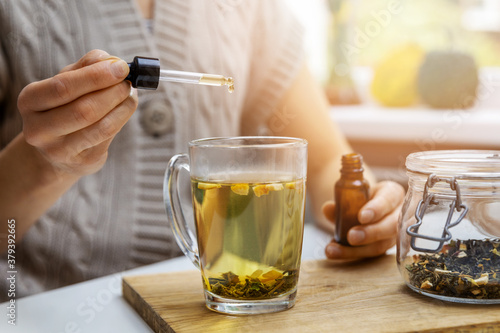 dietary supplements and vitamins - woman adding drop of cbd oil in cup of tea with pipette. anti stress photo