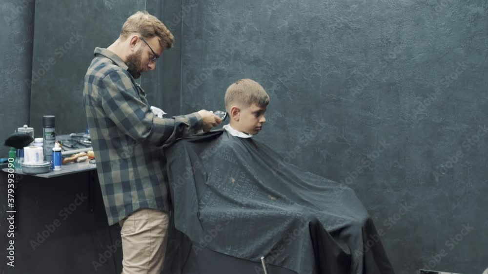 Men's haircut in Barbershop. Close-up of master clipping a man's hair with clipper. Teenager boy came to Barbershop to have hairstyle Men's haircut in Barbershop. Close-up of master clipping a man's hair with clipper. Teenager boy came to Barbershop to have hairstyle