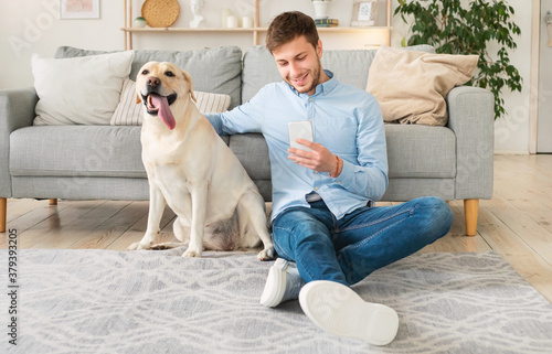 Portrait of young guy with his dog using mobile phone