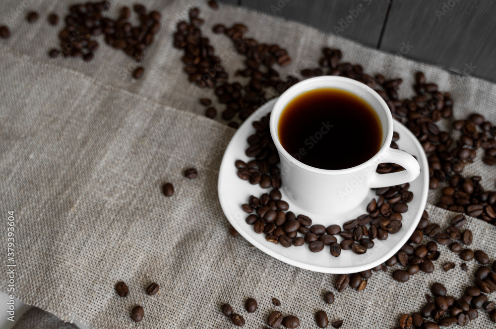 Fototapeta premium Coffee cup with roasted coffee beans on linen background. Mug of black coffe with scattered coffee beans. Fresh coffee beans.