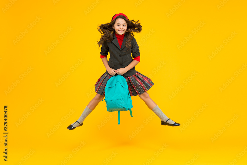 Happy small kid in formal uniform hold school bag jumping in midair yellow background, schooling