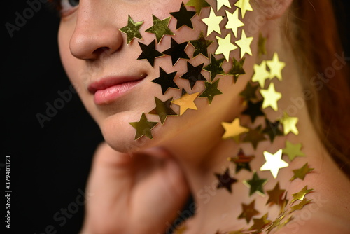 Beautiful young woman face close up portrait in studio on black. various emotions. foil stars glued to the face