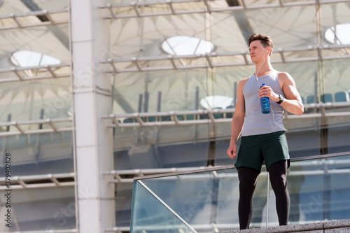 Athlete handsome man relaxing and drink water, modern stadium building background