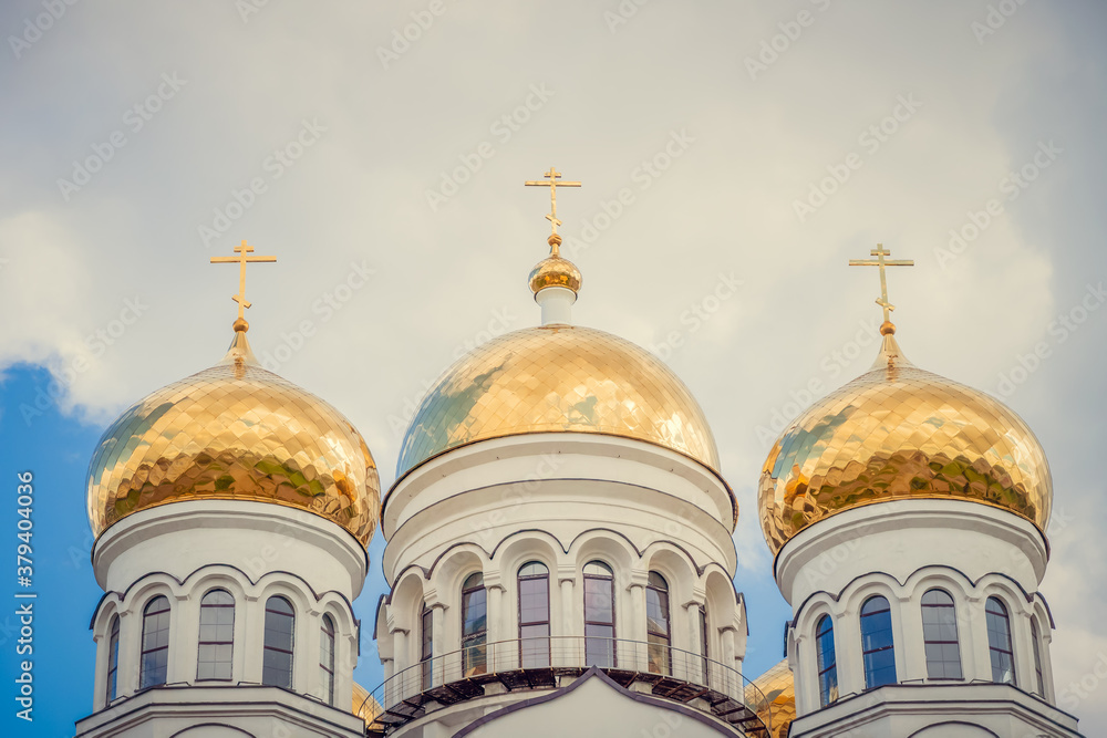 Golden domes, cupolas with Eastern Orthodox crosses on a white Church against a blue sky with clouds Golden domes, cupolas with Eastern Orthodox crosses on a white Church against a blue sky with clouds