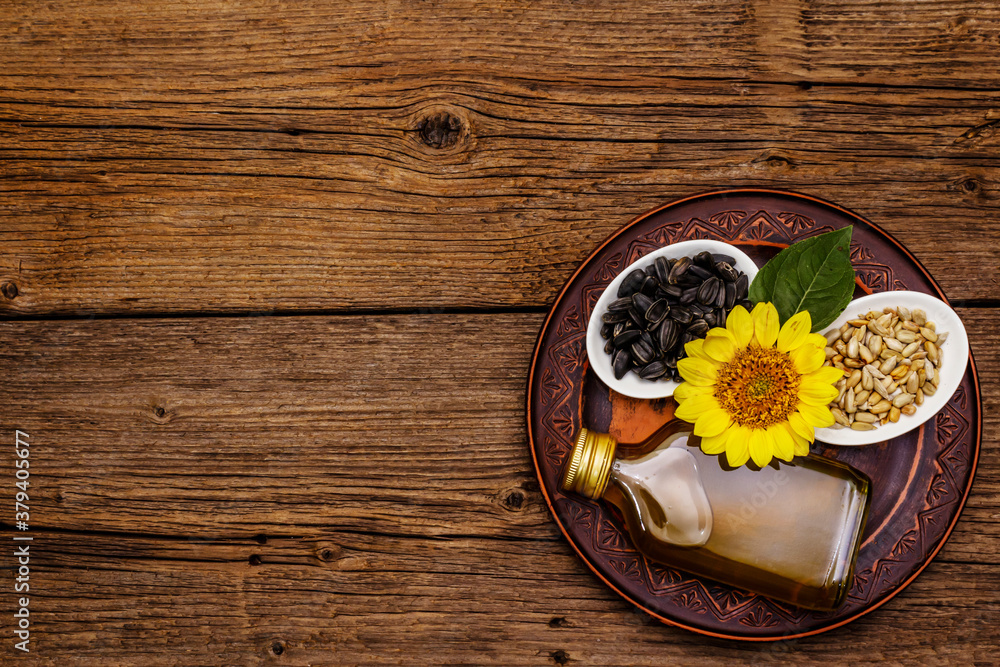 Sunflower oil in glass cruet with flower head and seeds in wooden bowl Sunflower oil in glass cruet with flower head and seeds in wooden bowl