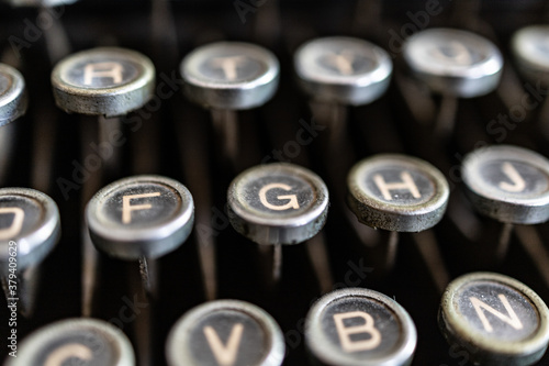 Selective focus close up on the keys of a black, vintage typewriter of the past century. Focus on F and G letters, blurred background.