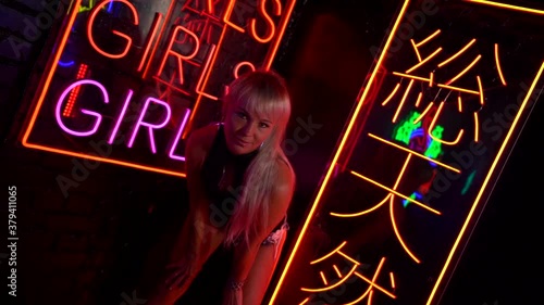 seducing young woman in nightclub, posing against wall with neon lights, flirt and temptation photo