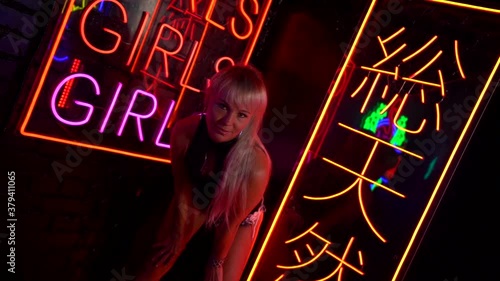 seducing young woman in nightclub, posing against wall with neon lights, flirt and temptation