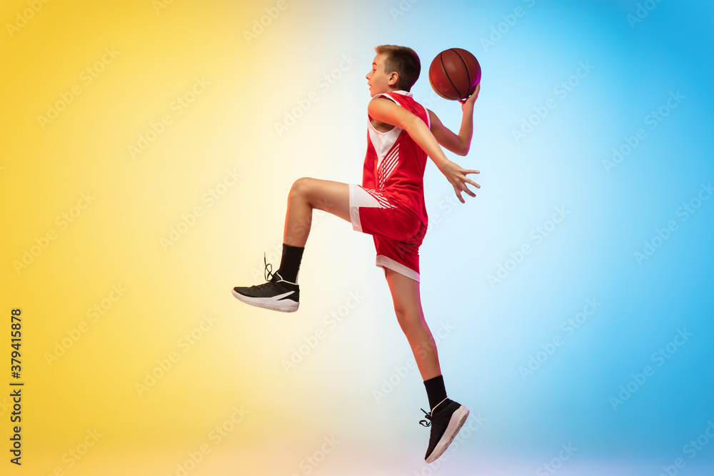 Jump high. Full length portrait of young basketball player in uniform on gradient studio background. Teenager confident posing with ball. Concept of sport, movement, healthy lifestyle, ad, action