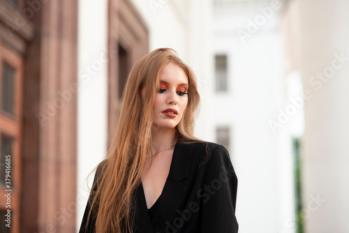 Free Download A girl with red hair, dressed in a black jacket, posing against the backdrop of a white building. Looking away. - GFXLoad