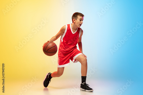 Hurry up. Portrait of young basketball player in uniform on gradient studio background. Teenager confident practicing with ball. Concept of sport, movement, healthy lifestyle, ad, action, motion.