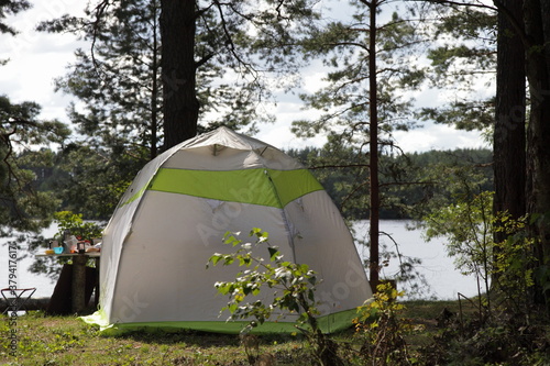 White dome camping tourist tent in the forest on beautiful Bank of Volga river on a Sunny summer day, weekend outdoor active tourism