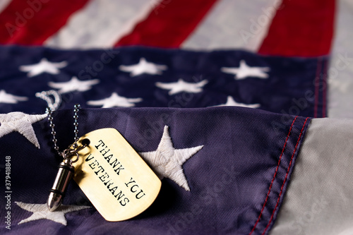 Closeup of a dog tag with the text thank you veterans on a flag of the United States background.