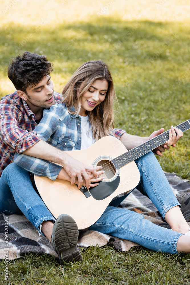 woman sitting on blanket and playing acoustic guitar with boyfriend
