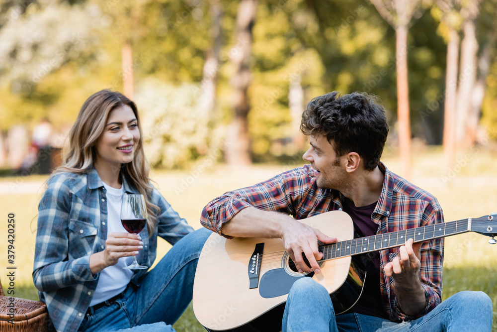 Fototapeta premium woman holding glass of red wine and looking at man playing acoustic guitar
