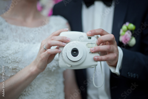 Newlyweds are holding a polaroid camera. Selective focus