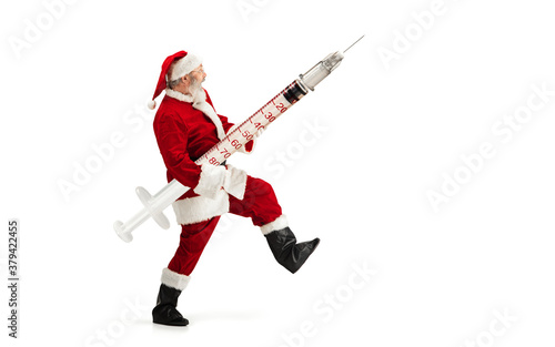 Santa Claus holding huge vaccine against COVID like Christmas gift isolated on white background. Male model in traditional costume. New Year, holidays, winter, epidemic, pandemic concept. Copyspace.