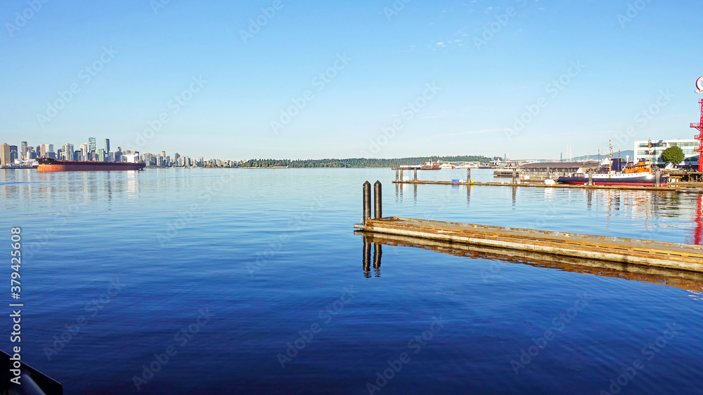 Fototapeta premium Jetty reflected on tranquil waters at Lonsdale Quay, BC, with Vancouver waterfront and Stanley Park on horizon
