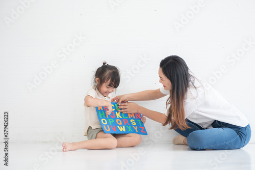Young Asian mother taught her little daughter about reading English characters, having fun together, family concept