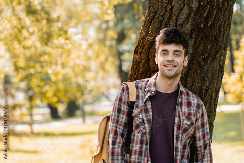 man in checkered shirt looking at camera near tree trunk in park