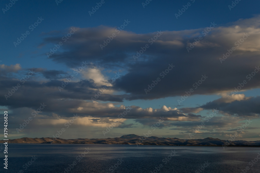 Fototapeta premium view of the clear calm undulating blue water of Lake Baikal, mountains on the horizon, evening, sunset clouds