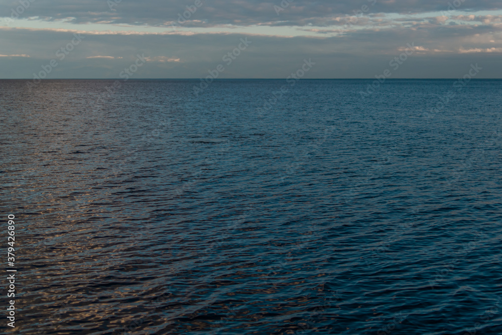 Obraz premium view of the clear calm undulating .ripples water of Lake Baikal, sunset clouds on the horizon, sky background