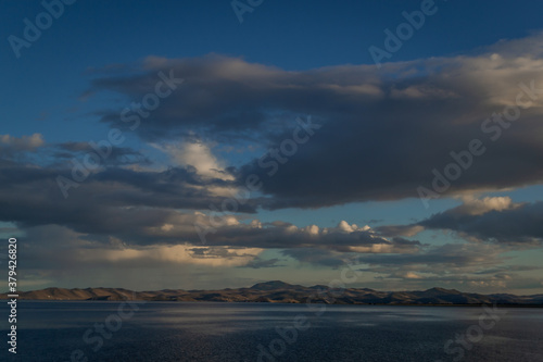 view of the clear calm undulating blue water of Lake Baikal, mountains on the horizon, evening, sunset clouds