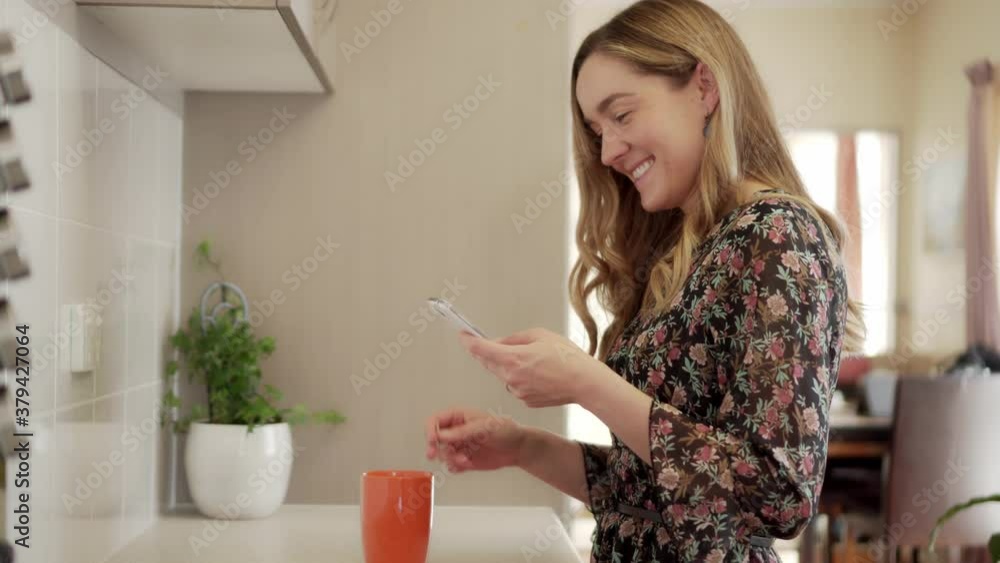Laughing girl swipes smart phone while making cup of tea in kitchen, dolly shot Laughing girl swipes smart phone while making cup of tea in kitchen, dolly shot