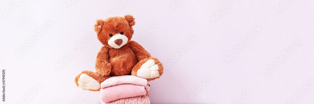 Brown stuffed teddy bear sitting on stack of clean cotton towels or clothes. Childhood care, clothing and plush toy for children in orphanage. Doll for nursery or charity. Website banner, web page