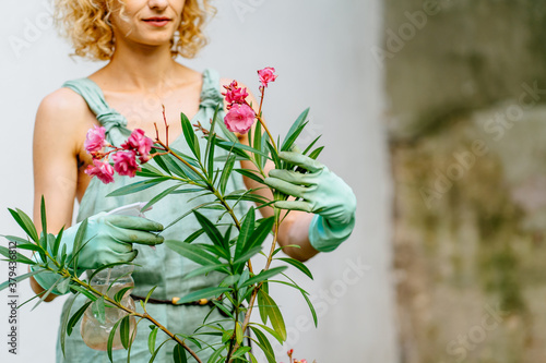 Positive charming female gardener wear mint gloves caressing blooming oleander tree in pot at backyard, outdoor. Change of activity the best rest. photo