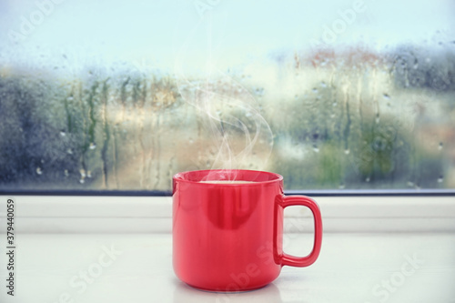 Cup of delicious hot drink on window sill after rain