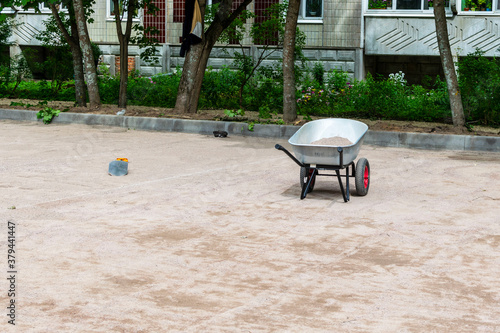 A wheelbarrow with sand near the house on the sidewalk.