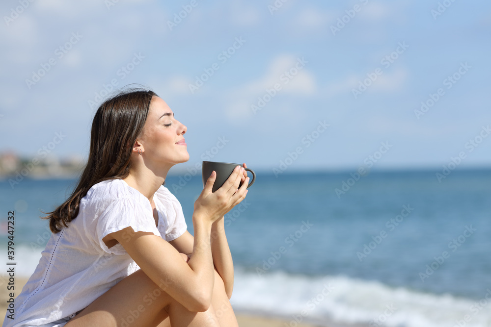 Girl smelling coffee on the beach on summer