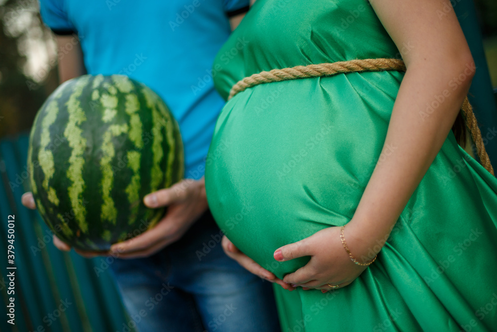 A pregnant woman and a man are holding a watermelon.Young beautiful pregnant couple with