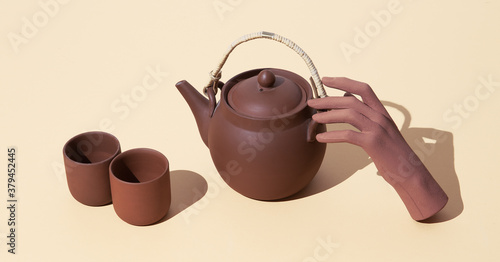 Fake hand holding clay teapot on beige background. Minimal stilll life isometric art photo