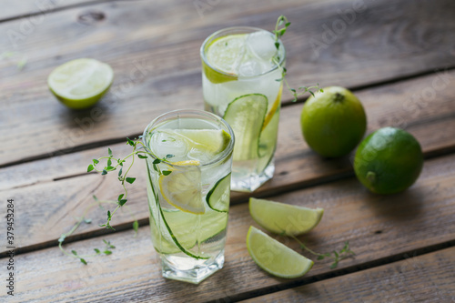 Summer alcoholic drink. Homemade refreshing cocktail with gin, vodka or tequila, cucumber, lime, ice cubes and thyme on a wooden background