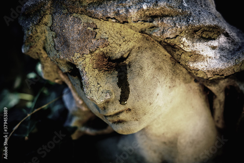 Close up ancient statue of crying angel with tears in face as symbol of death and end of human life. Selective focus on eyes.
