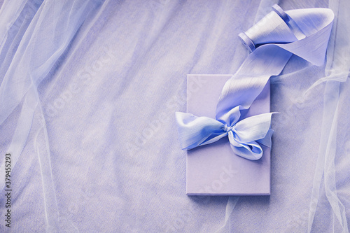 Gift boxes with hand dyed silk ribbon with bow on wood spool on purple fabric with folds background and copy space © AnaGost