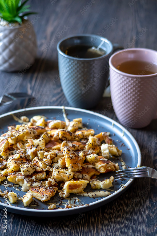 Fluffy, gluten-free, shredded pancake / kaiserschmarrn served with halvah spread, banana, walnuts, and grated chocolate placed on a decorative plate and teacups at the background Fluffy, gluten-free, shredded pancake / kaiserschmarrn served with halvah spread, banana, walnuts, and grated chocolate placed on a decorative plate and teacups at the background