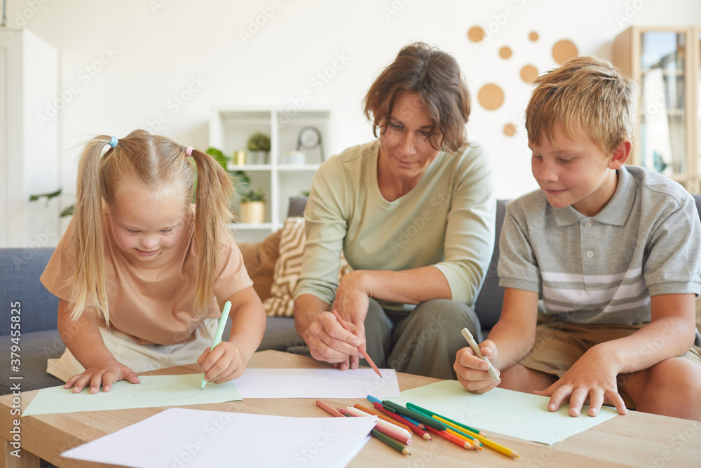 Portrait of cute blonde girl with down syndrome drawing with mother and brother together in home interior Portrait of cute blonde girl with down syndrome drawing with mother and brother together in home interior