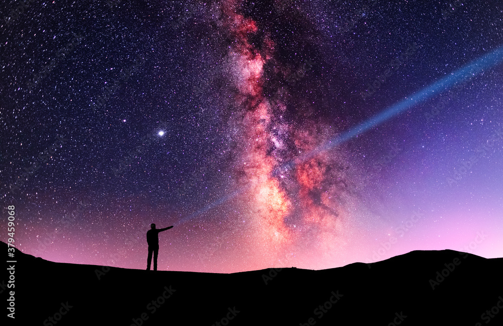 Beautiful starry sky with bright milky way galaxy. Night landscape . Person silhouette stands on the shore with flashlight illuminate starry sky.